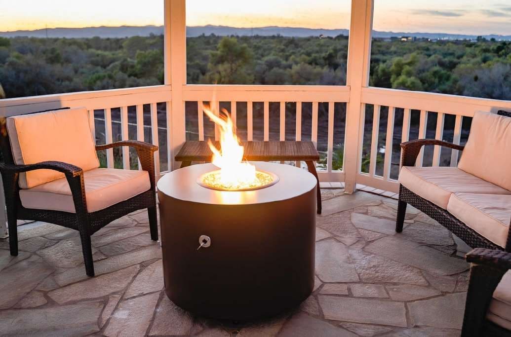 Fusion round cylindrical gas fire table in a matte dark finish, lit on a stone balcony at sunset