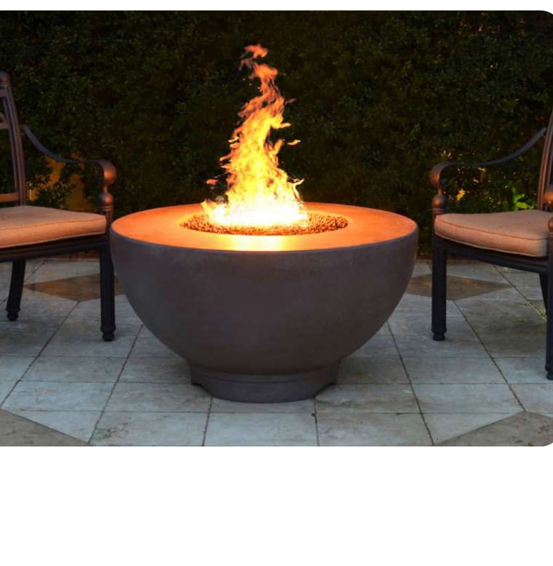 Inferno round concrete gas fire bowl with a tall flame, set between two outdoor armchairs